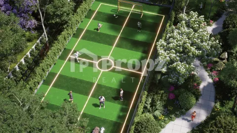 Illuminated football turf court surrounded by flowering trees and landscaped gardens